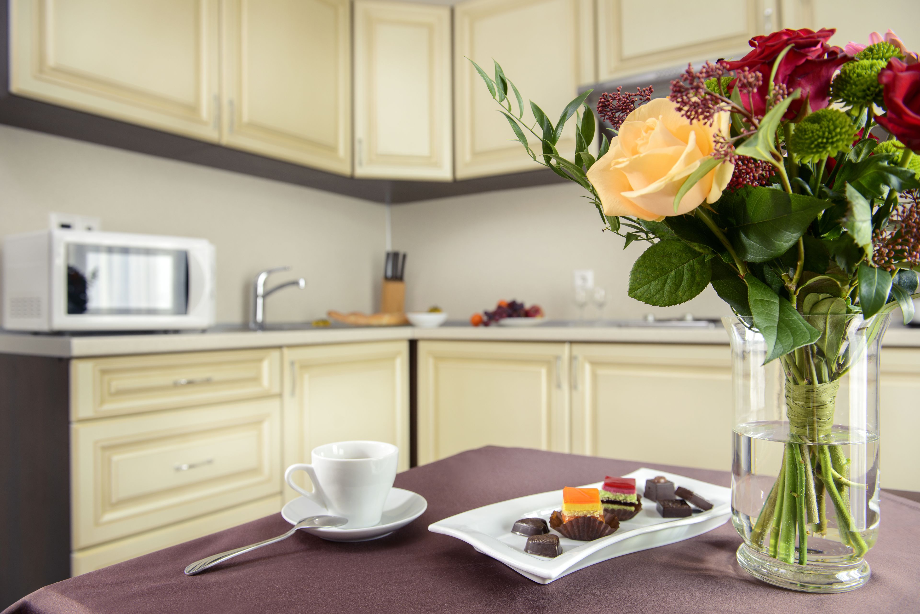 A dining table with a white cup, a plate of desserts, and a vase with flowers.