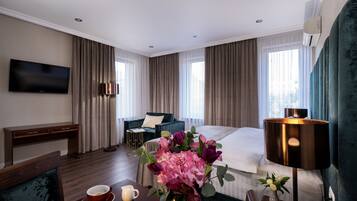A hotel room with a bed, a desk, a TV, a lamp, and a dining table with a vase of flowers.