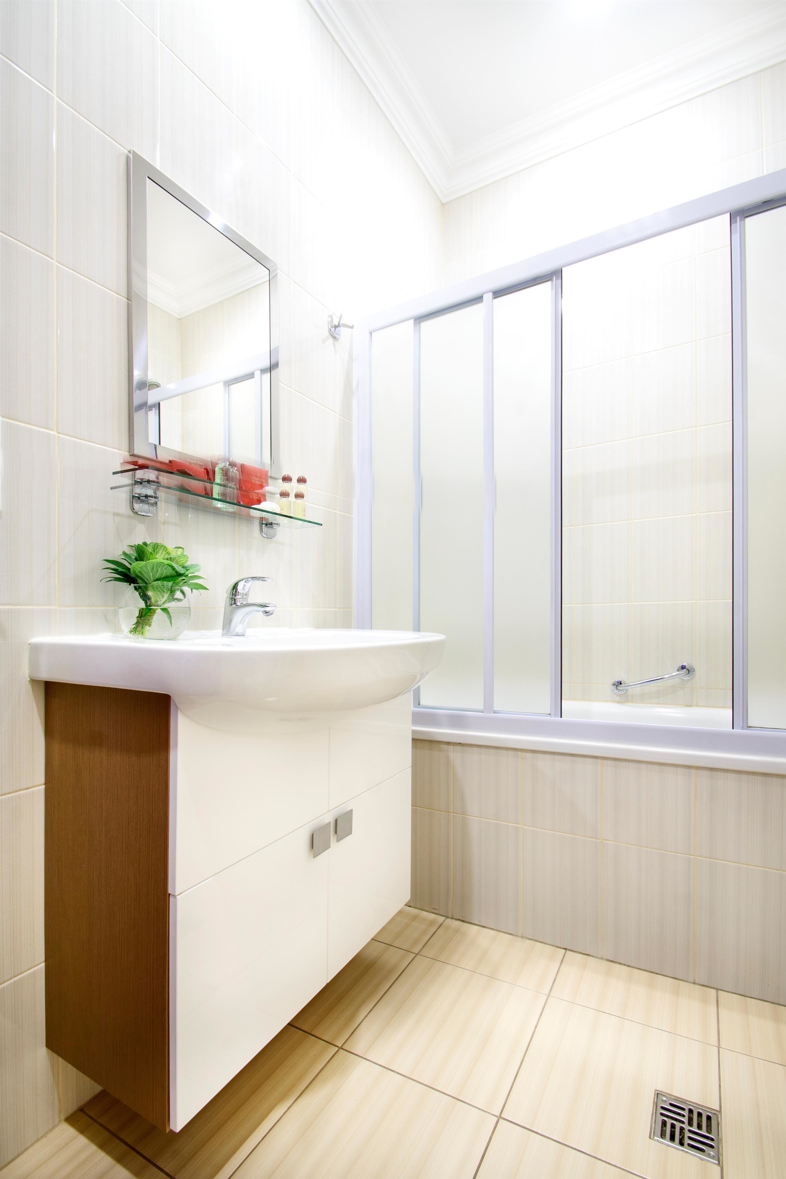 A modern bathroom with a white sink, mirror, and shower enclosure.