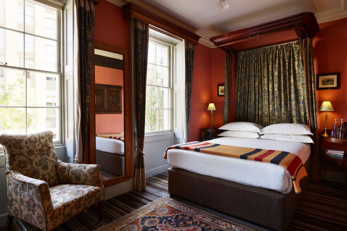 A hotel room with a large bed, a chair, a patterned rug, and curtains.