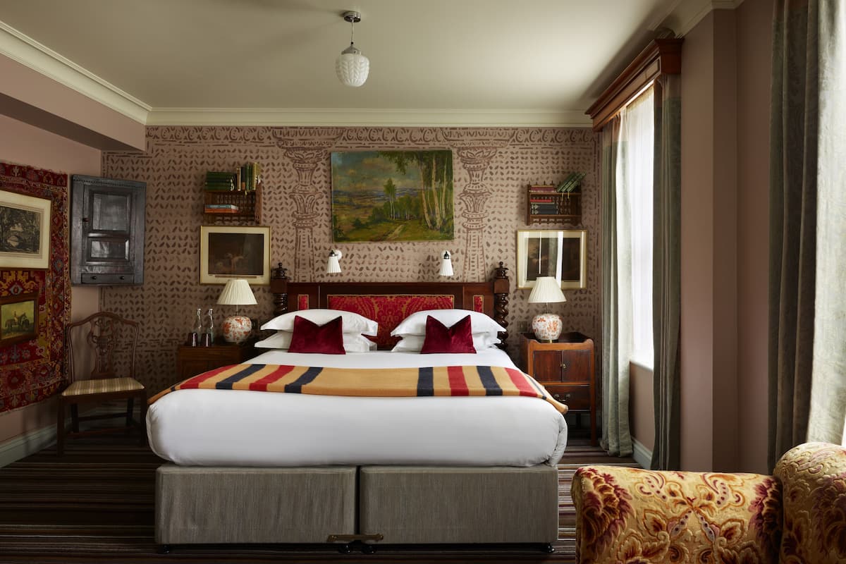 A hotel room with a large bed, two bedside tables, a chair, a painting on the wall, and a window with curtains.