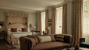A bedroom with a bed, a brown sofa, a bedside table, a lamp, and a window with curtains. - The Zetter Clerkenwell (London)