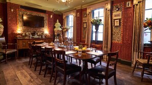 A dining area with a wooden table and chairs, a chandelier, and a television mounted on the wall. - The Zetter Clerkenwell (London)