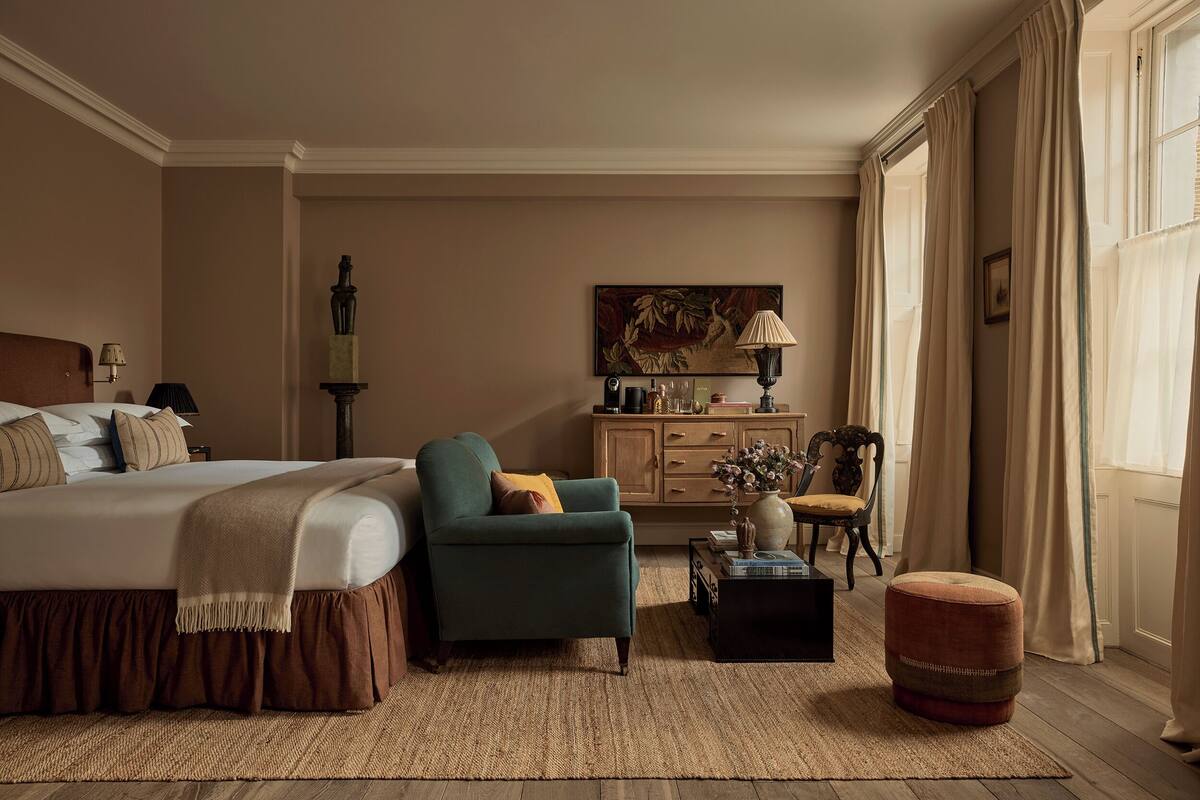A bedroom with a bed, a chair, a small table, a cabinet, and a window with curtains.