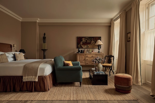 Un dormitorio con cama, una silla, una mesita, un armario y una ventana con cortinas.