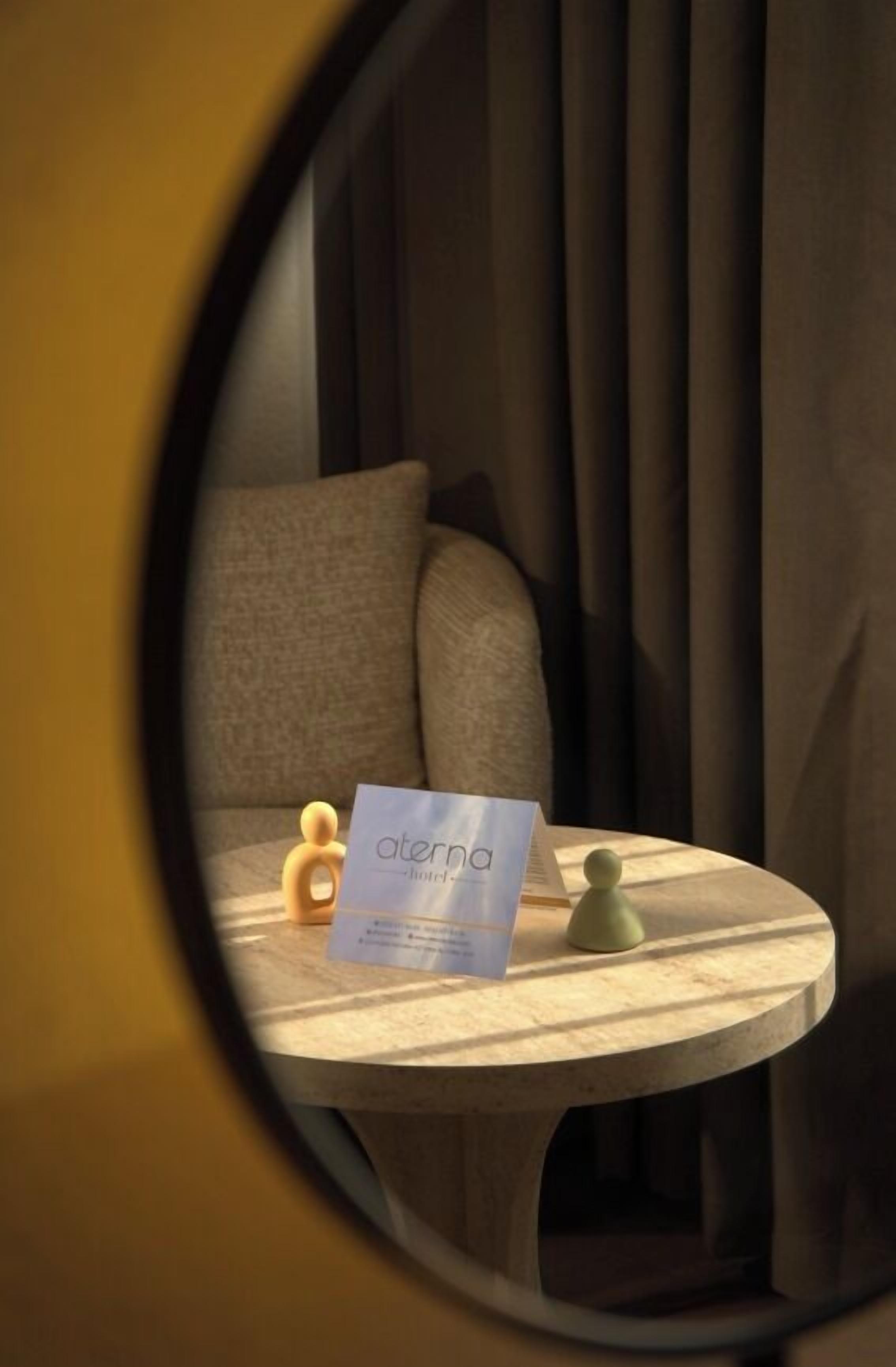A circular window view of a room with a bed, a small table with a card, and a wall with curtains.