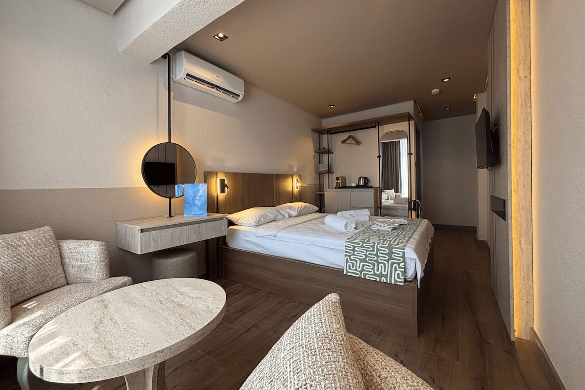 A hotel room with a bed, a round table, a sofa, a mirror, and an air conditioning unit.