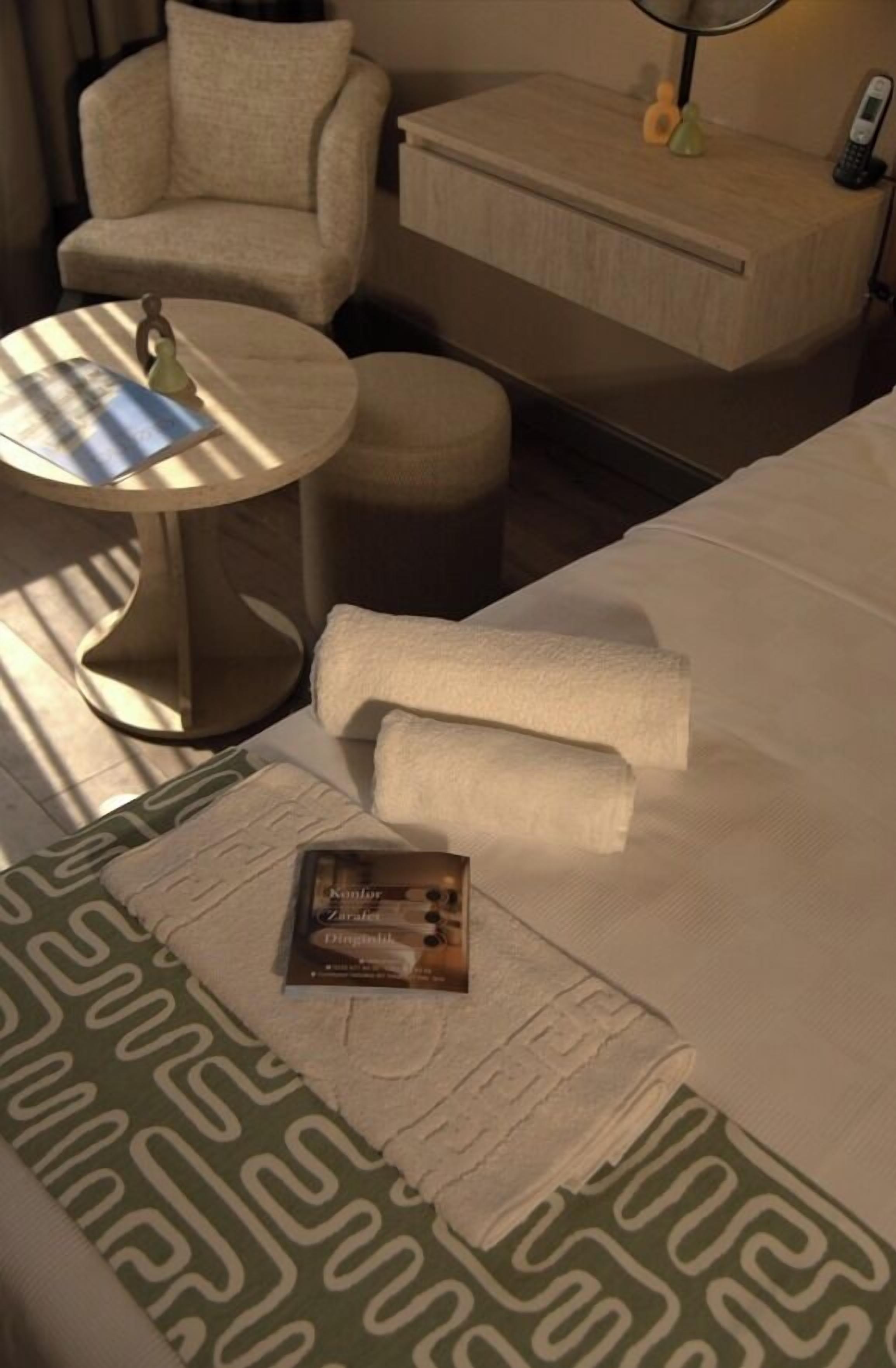A hotel room with a bed, a small round table, a chair, a bedside table, and a telephone.
