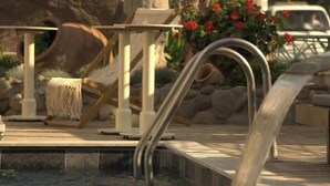 Une piscine avec un escalier en métal, un pilier en pierre et une chaise.