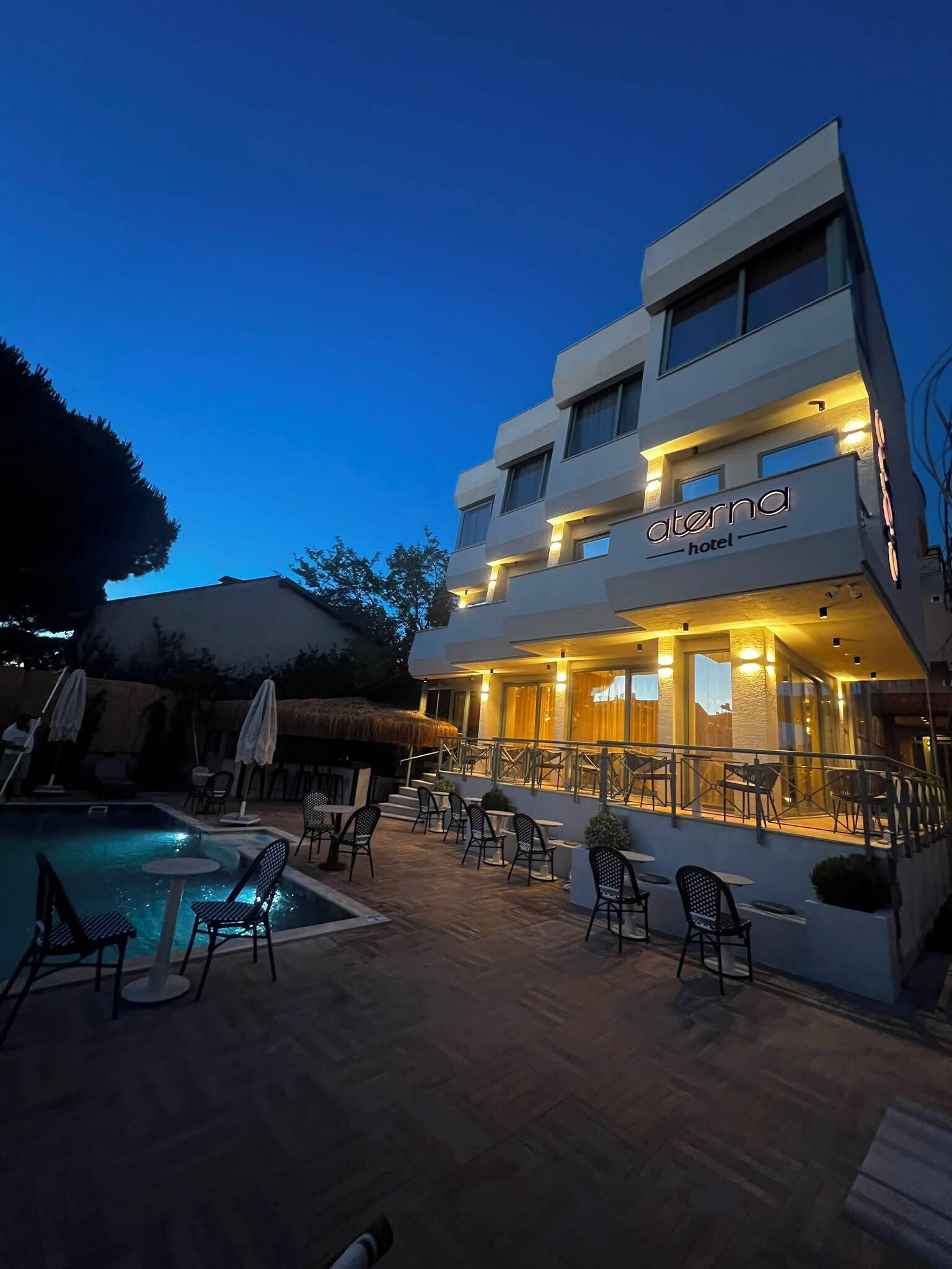 Un hotel con piscina, zona de estar exterior y una entrada bien iluminada.