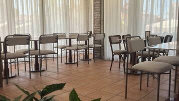 Un comedor con sillas y mesas, ventanas amplias con cortinas y piso de baldosas.