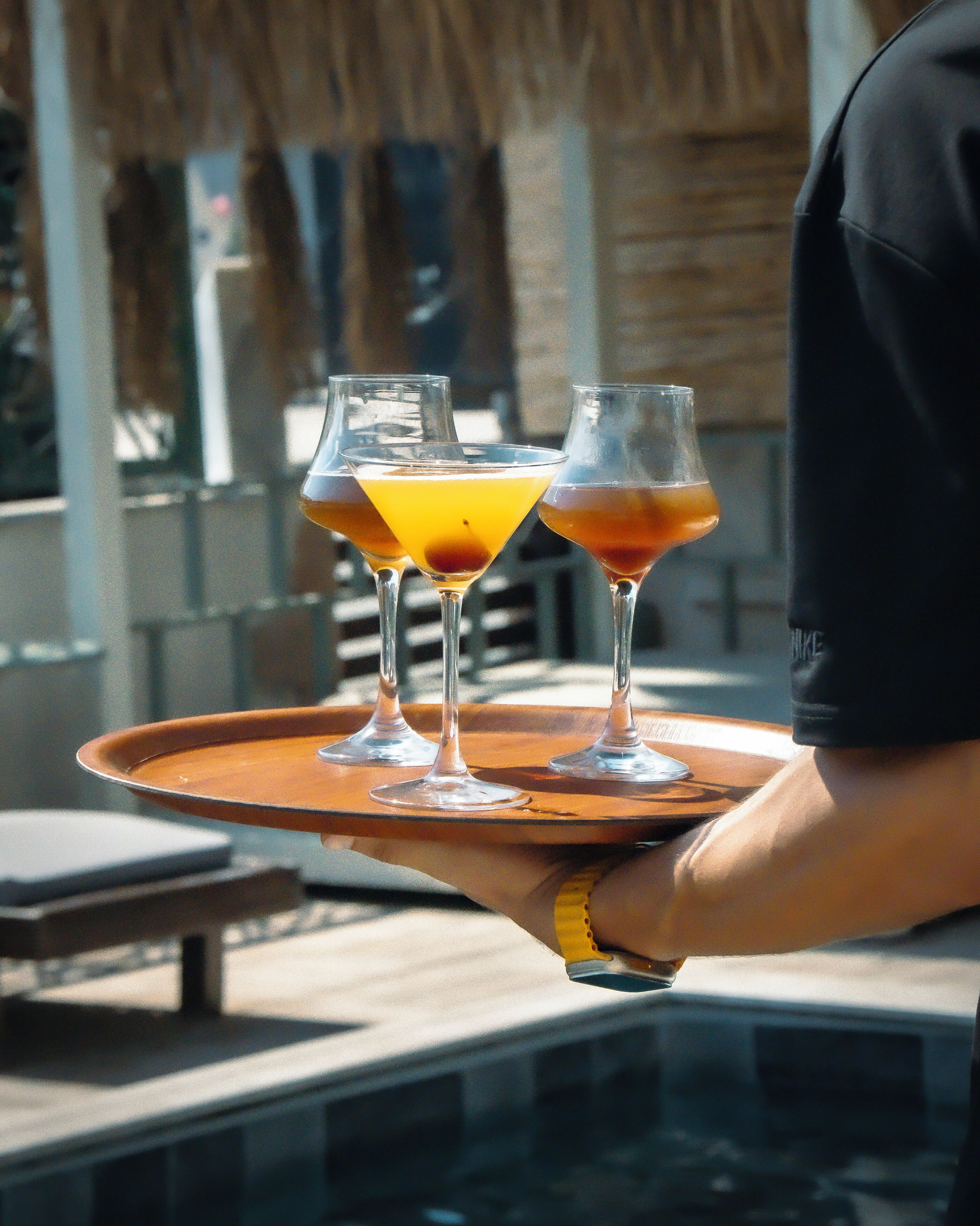 Une personne tenant un plateau sur lequel se trouvent trois verres contenant une boisson jaune-orangée.