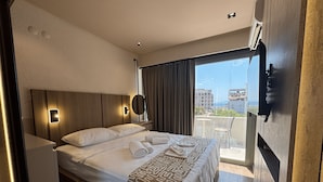 Une chambre d’hôtel équipée d’un lit, d’une table de chevet, d’un miroir et offrant une vue sur la ville grâce à de grandes fenêtres.