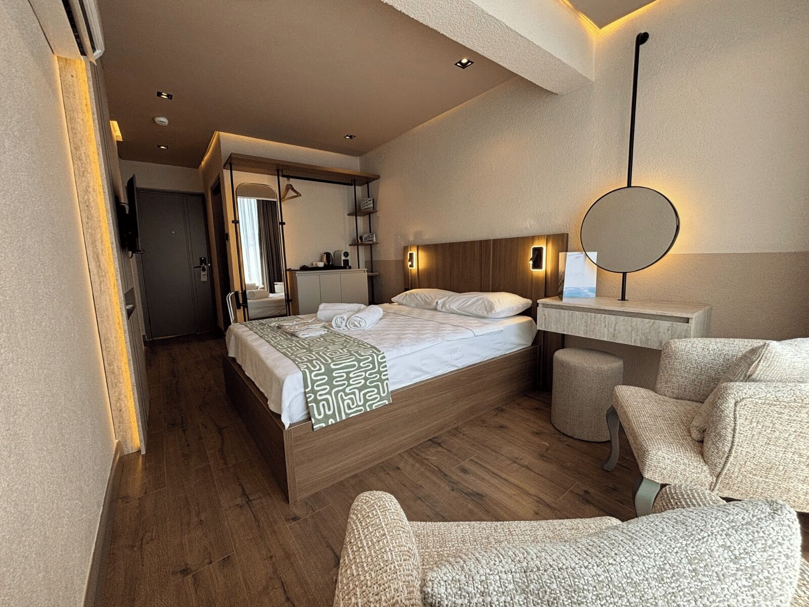A hotel room with a bed, bedside table, chair, and a mirror.