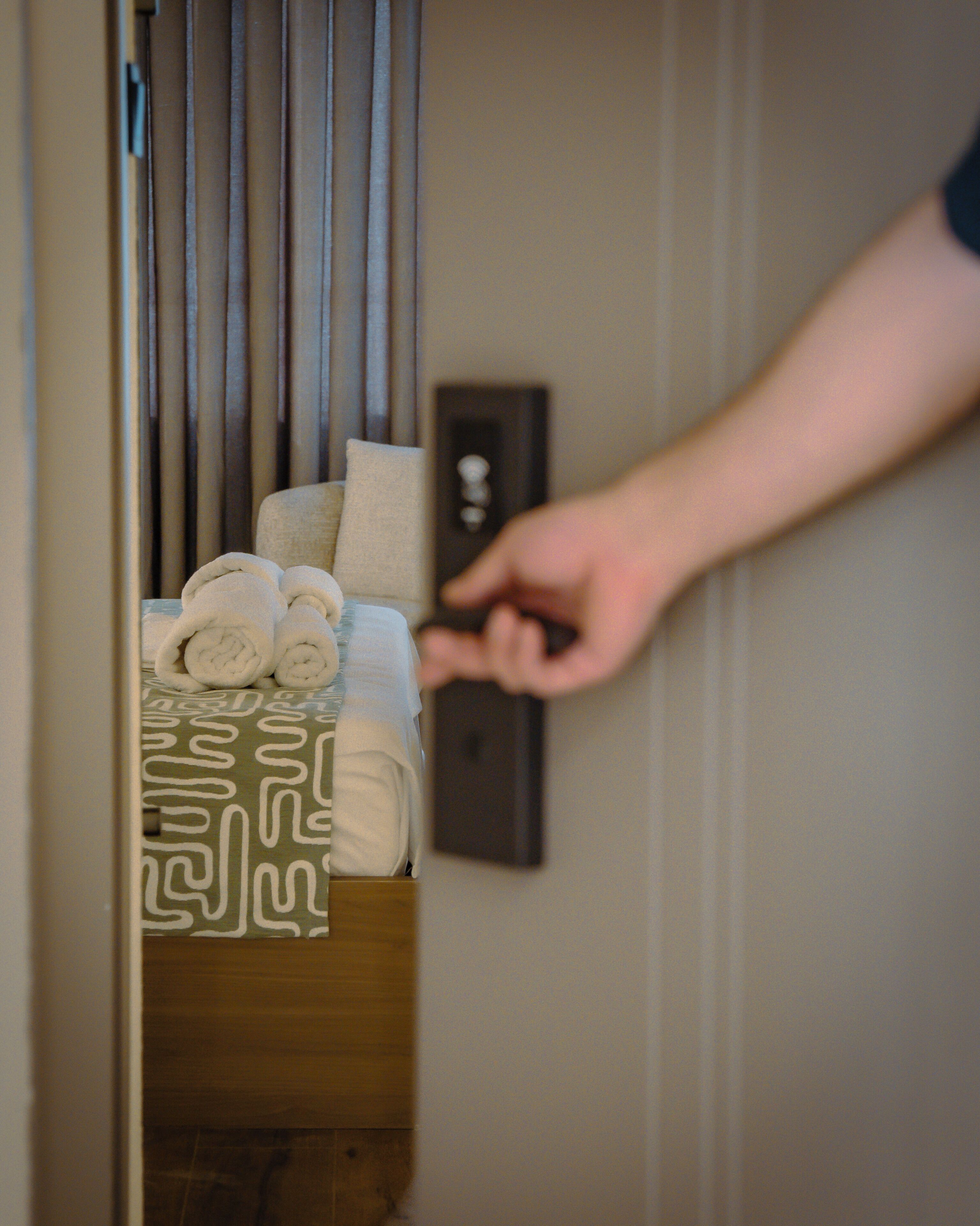 A hand reaching for a towel from a wooden storage unit in a hotel room.