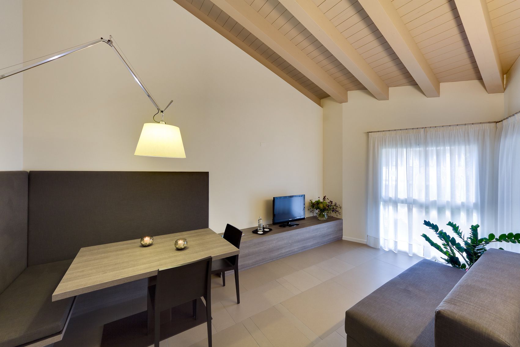 A modern living room with a wooden dining table, a sofa, a TV, and a lamp.