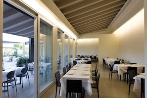 A restaurant with a long dining table, glass partitions, and a view of the outdoor patio area.