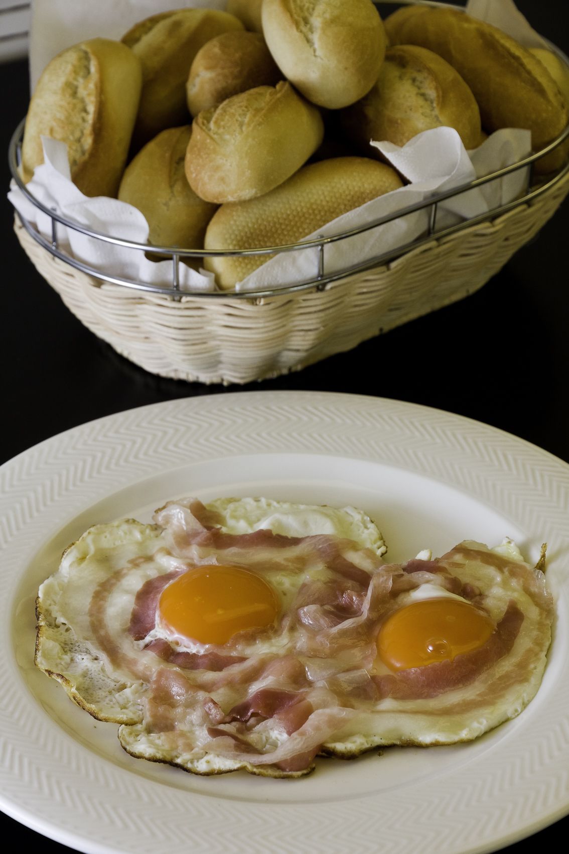 Une assiette avec deux œufs au plat et, au fond, un panier de petits pains.