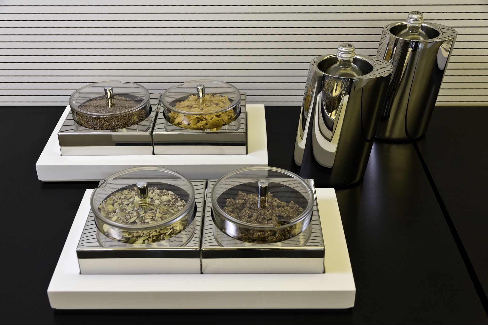 Una cocina con cuatro recipientes de vidrio sobre una encimera blanca, cada uno con tapa metálica.