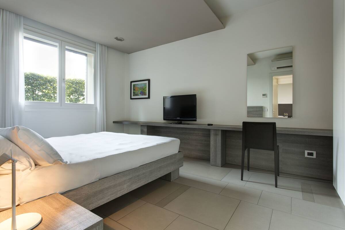 Un dormitorio moderno con cama, mesita de noche, televisor y una silla.