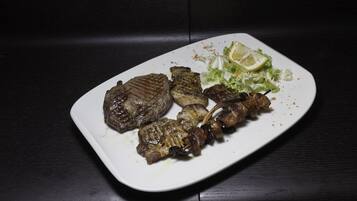 A plate of grilled meat with a side of lettuce and a slice of lemon on a white plate.