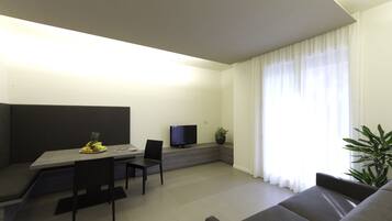 A modern living room with a sofa, a dining table with chairs, a flat-screen TV, and a potted plant.