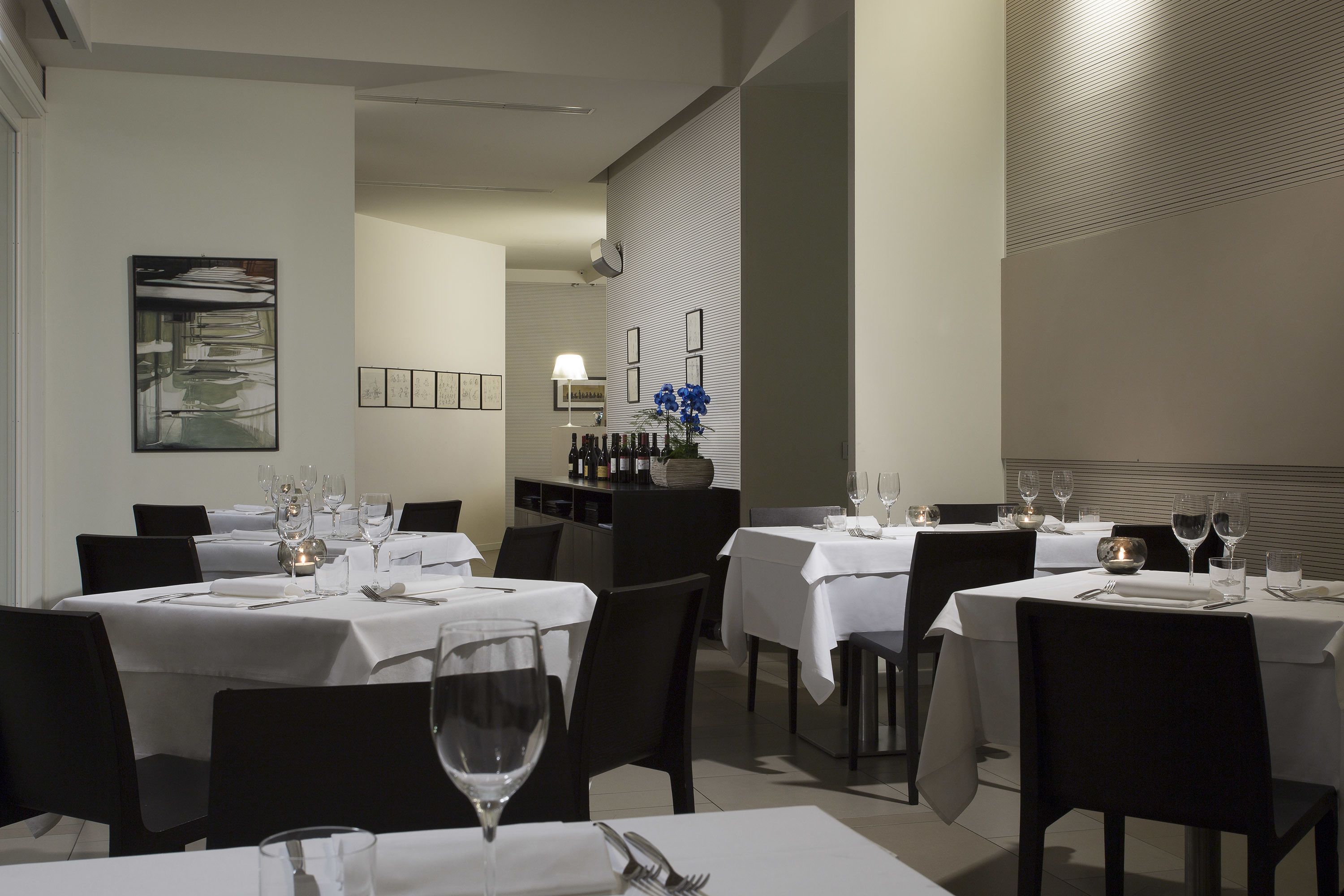 Un restaurante con varias mesas dispuestas para comer, cada una con manteles blancos y sillas negras.