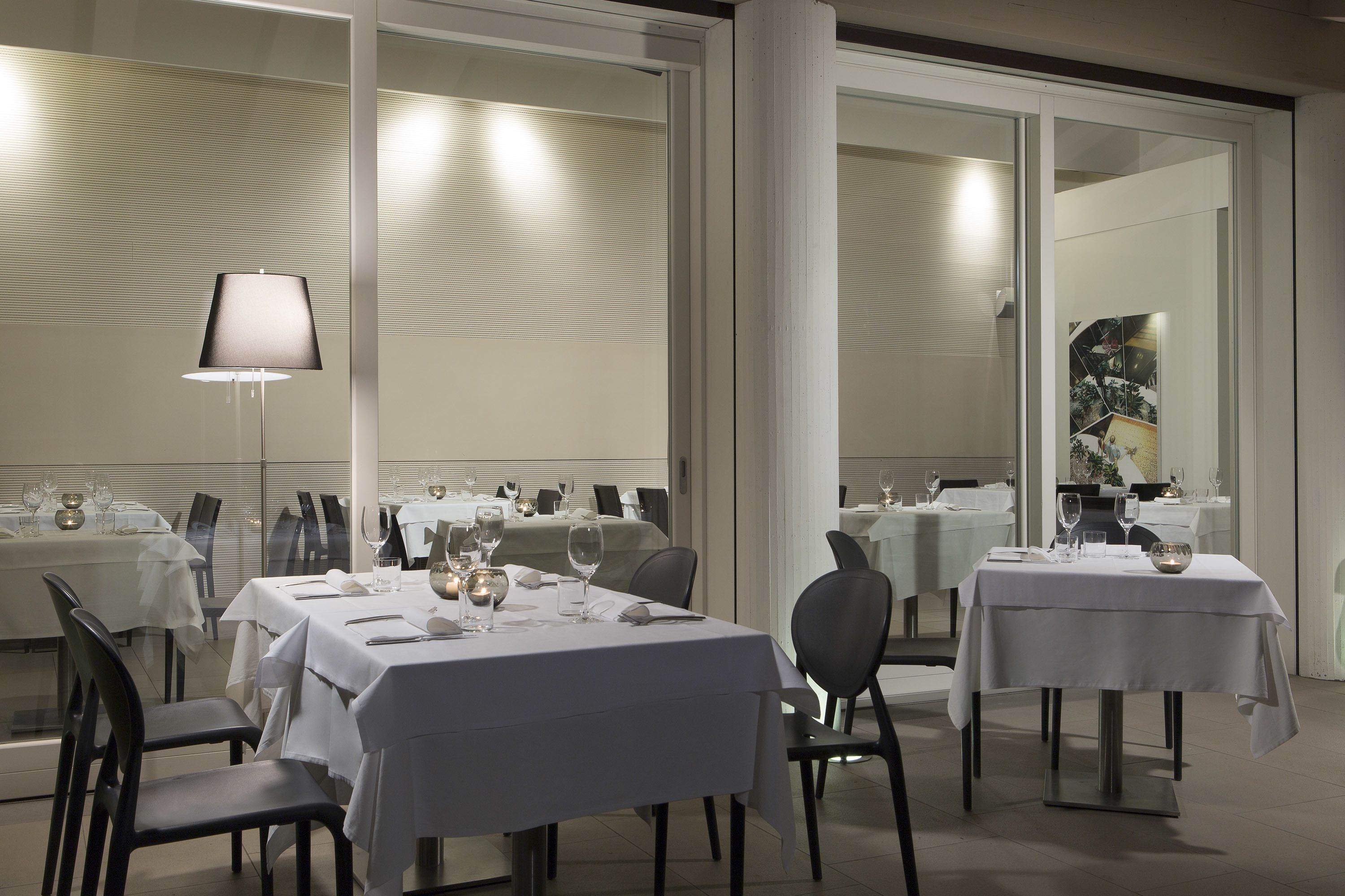 A restaurant with multiple tables set for dining, featuring white tablecloths and black chairs.