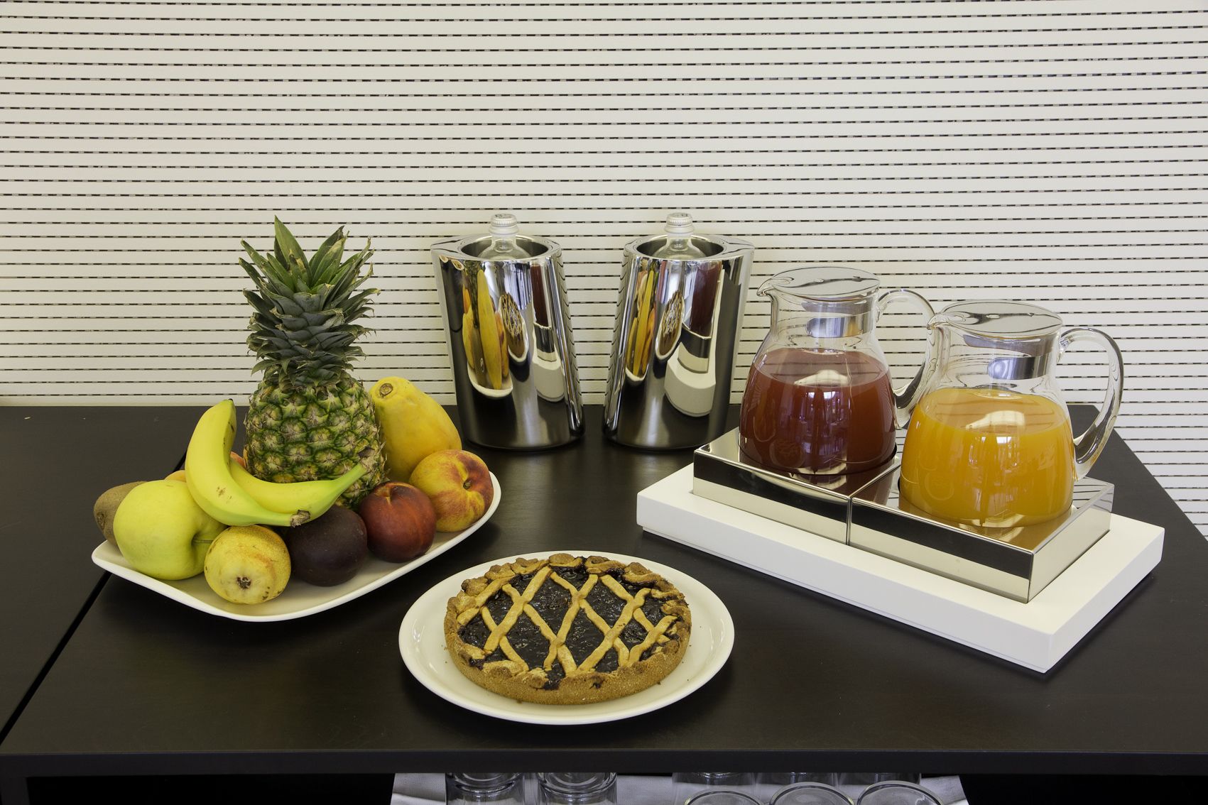 Un tavolo con un piatto di frutta, una crostata e un vassoio con una brocca e delle tazze.