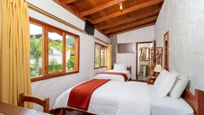 Una habitación con dos camas, muebles de madera y ventanas grandes con cortinas.