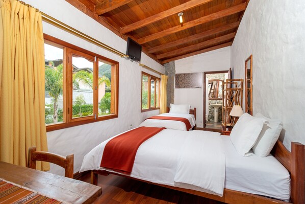 Una habitación con dos camas, muebles de madera y ventanas grandes con cortinas.