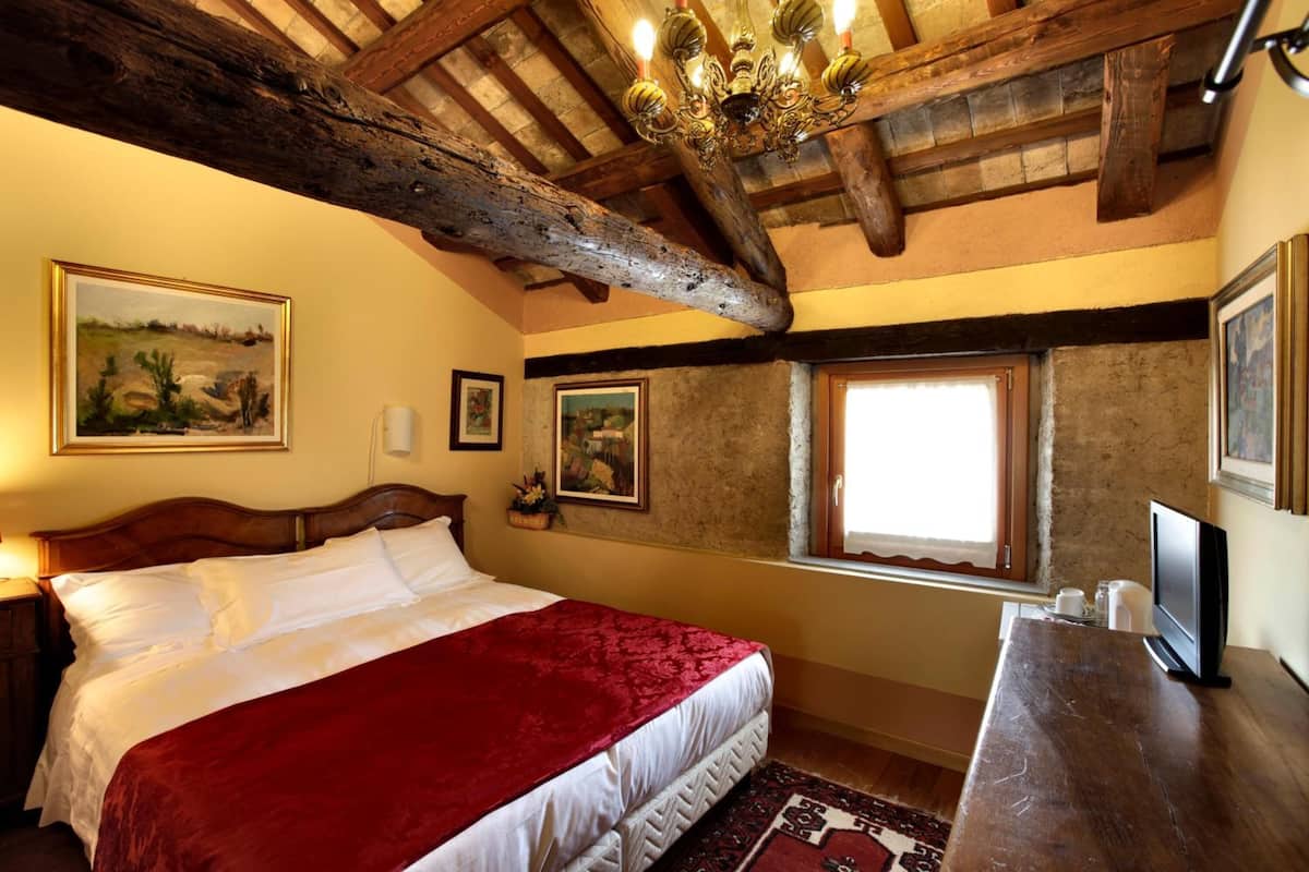 Quarto com uma cama grande, vigas de madeira, um candelabro e obras de arte emolduradas nas paredes.