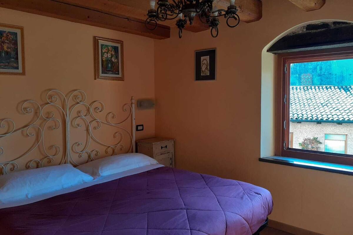 Quarto com cama, lustre, janela e duas imagens emolduradas na parede.