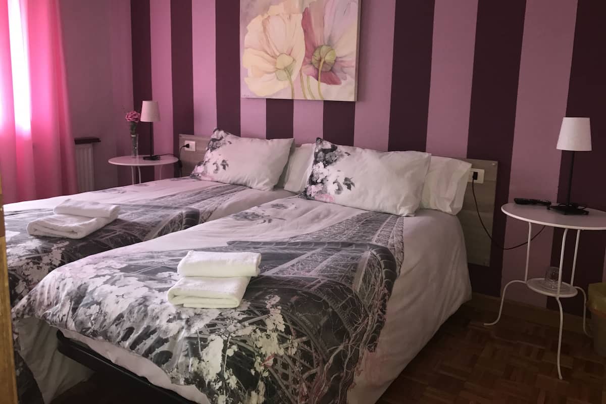 Ett hotellrum med två sängar, en blomstermålning på väggen och ett litet bord med en lampa.