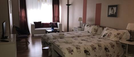 A hotel room with a large bed, a sofa, a desk with a computer, and a chair.