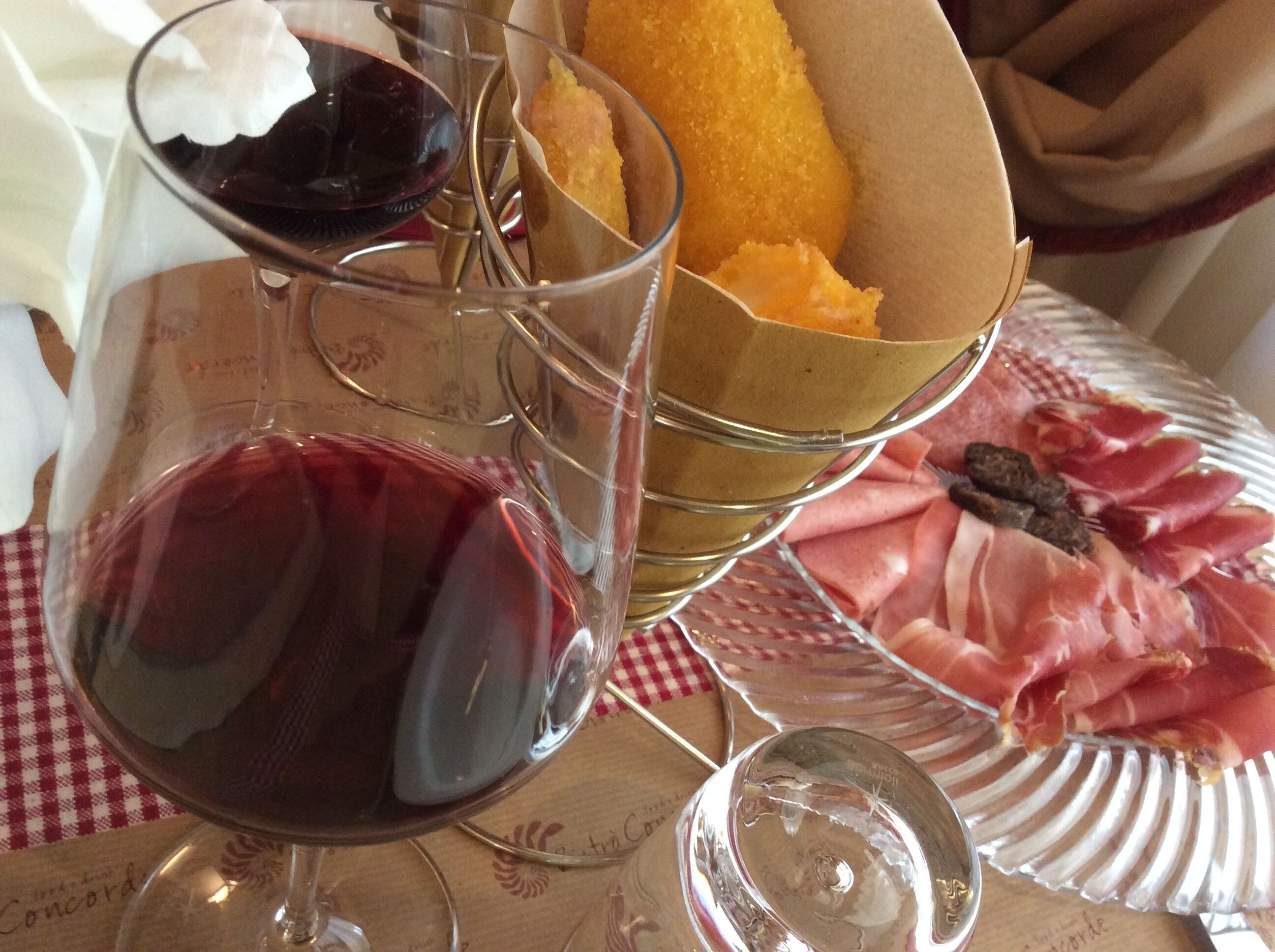 A table with a glass of red wine, a basket of bread, and a plate of cured meats.