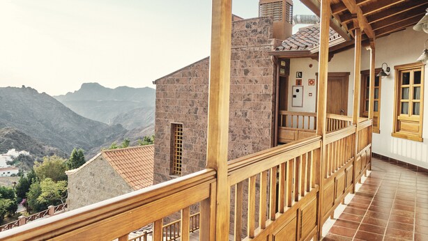 A wooden balcony with a stone building in the background, a tiled roof, and a mountainous landscape. - Hotel Rural Fonda de la Tea (Tejeda)