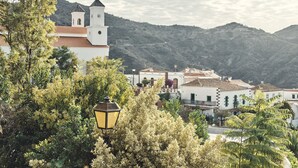 A white building with a bell tower, surrounded by greenery and hills in the background. - Hotel Rural Fonda de la Tea (Tejeda)