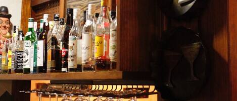Una zona de bar con vigas de madera, diversas botellas de licores y copas de vino.