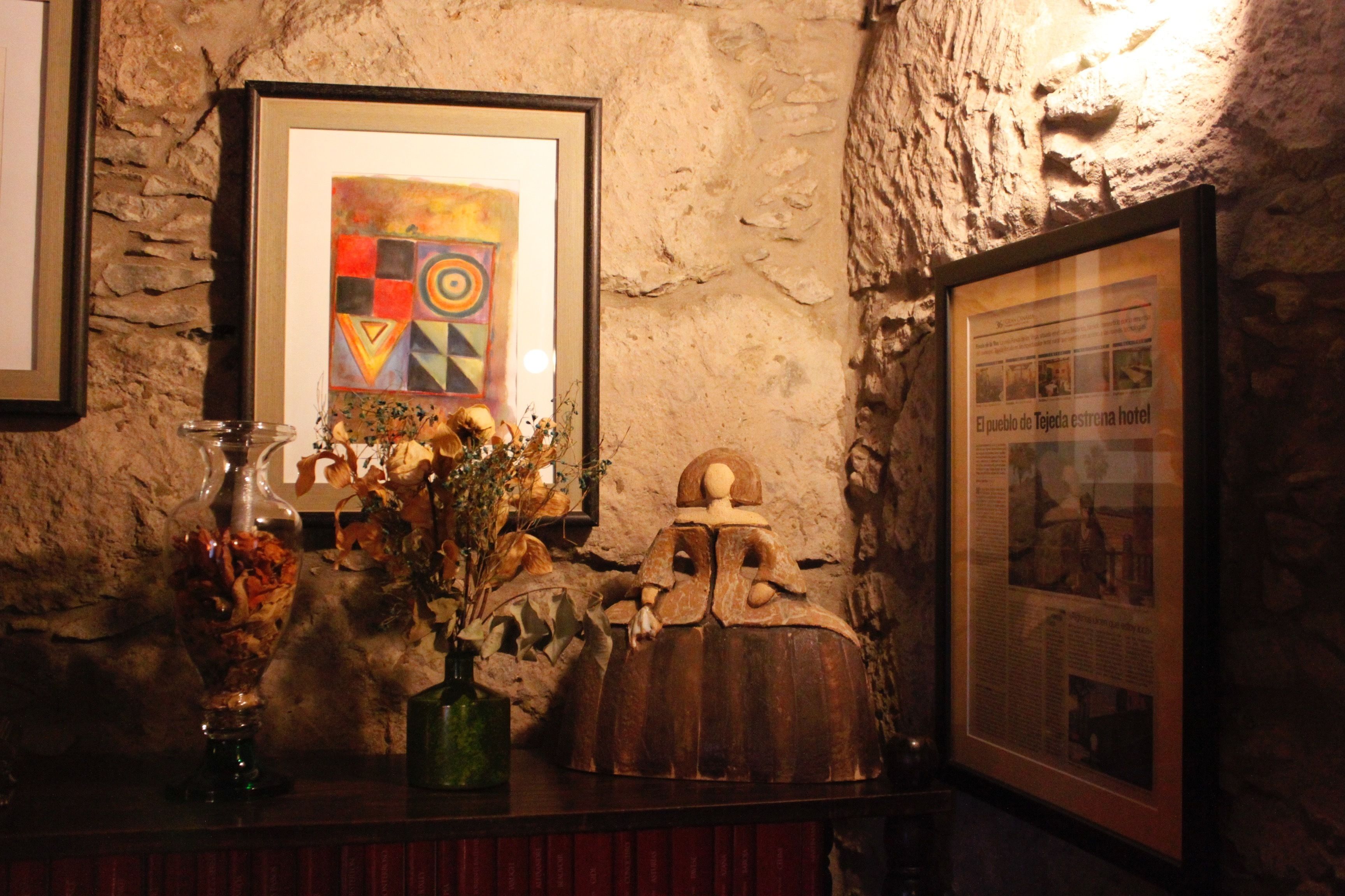 A stone wall with a framed abstract painting, a wooden sculpture, and a framed informational poster.