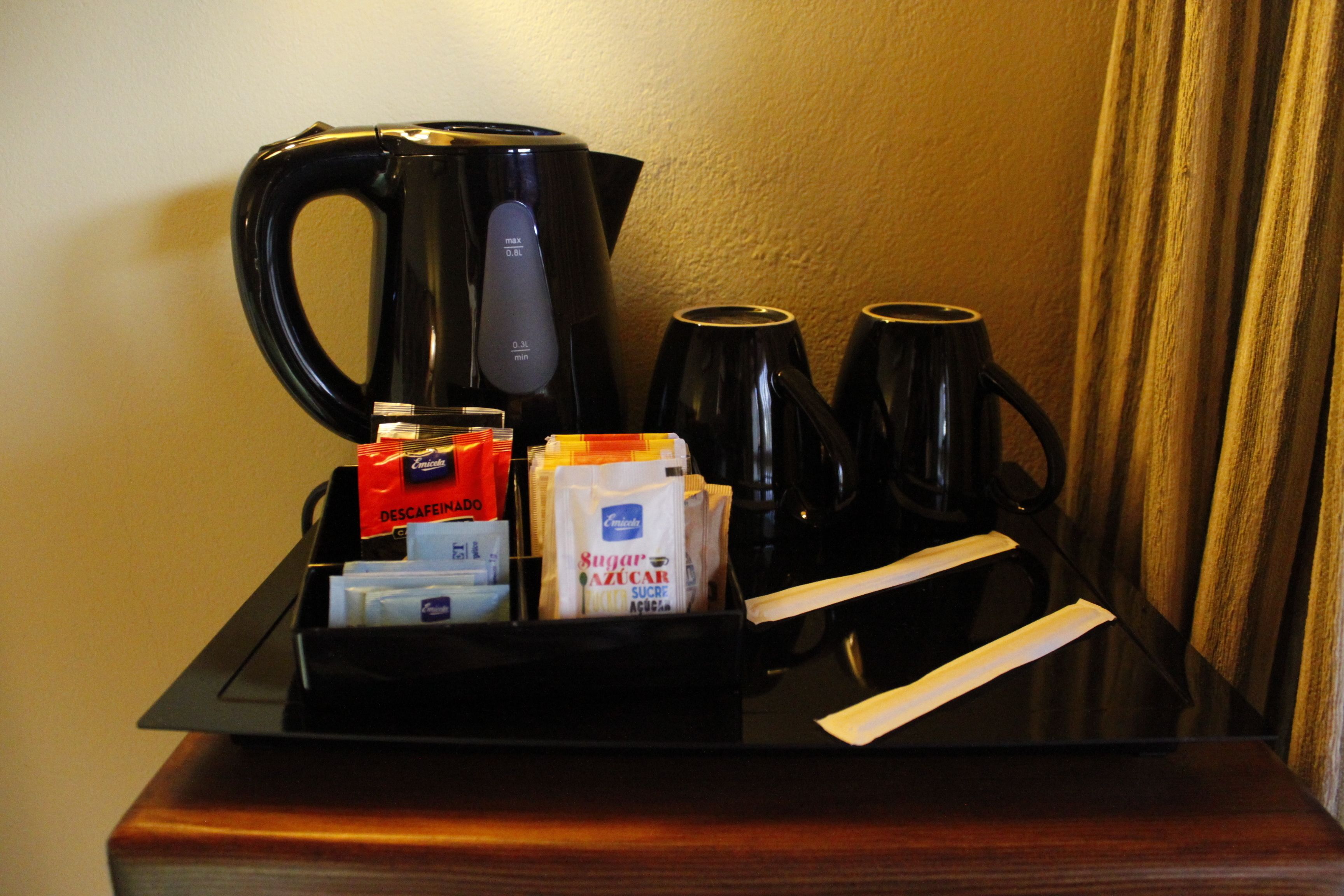 A coffee station with a coffee maker, cups, and sugar packets.