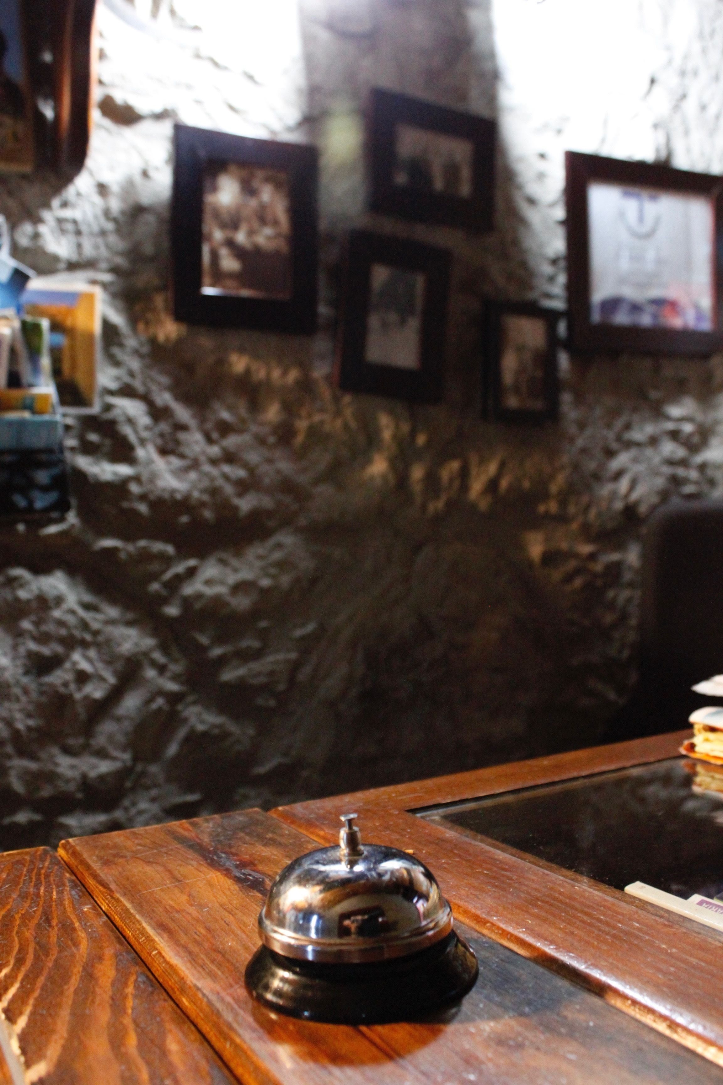 A wooden reception desk with a bell, framed pictures on the wall, and a stone wall.