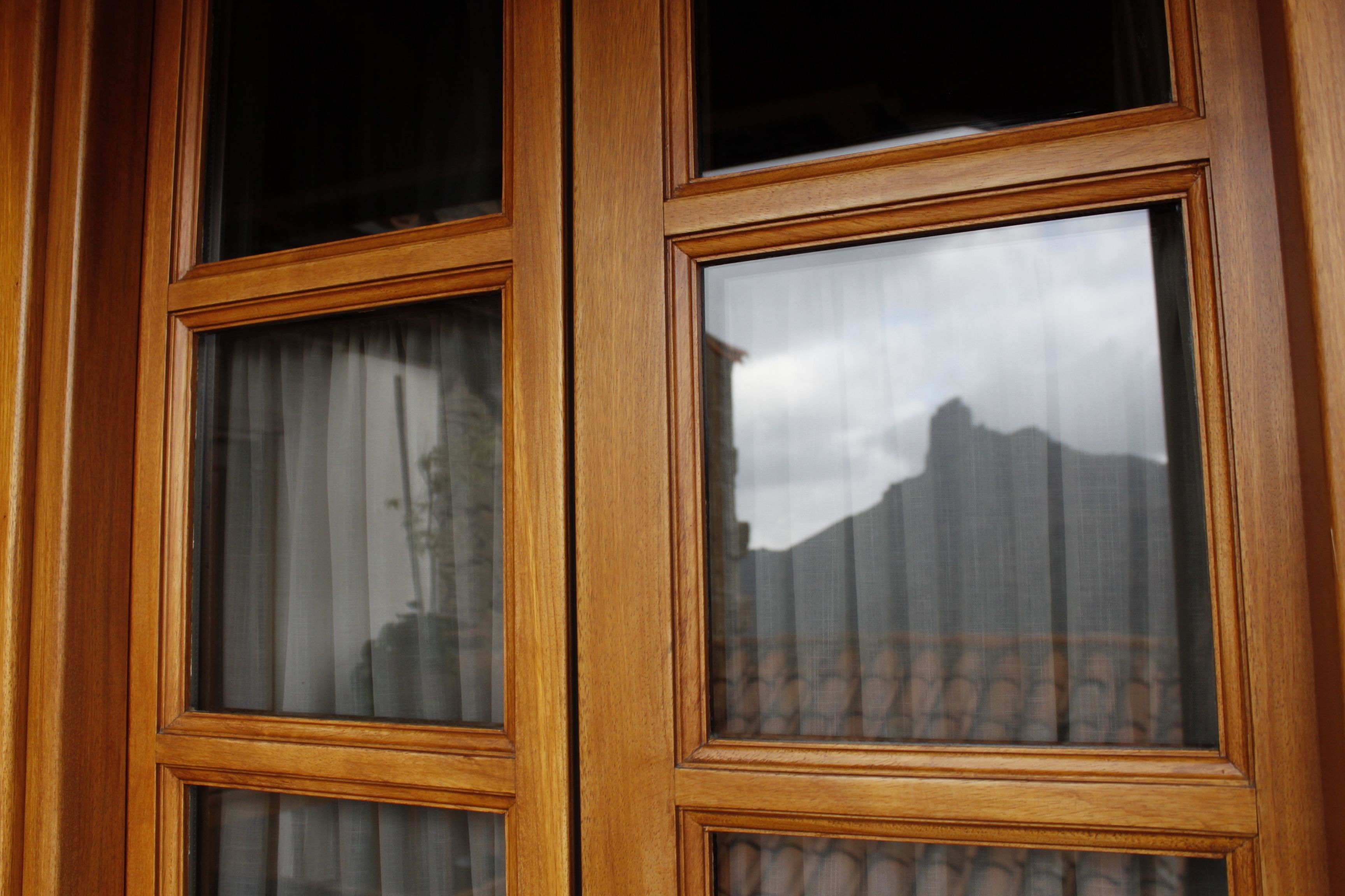 A wooden-framed window with multiple panes, reflecting a mountainous landscape and a building with a patterned roof.
