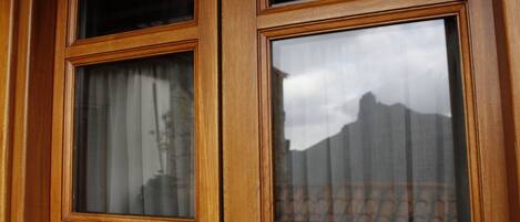A wooden-framed window with multiple panes, reflecting a mountainous landscape and a building with a patterned roof.