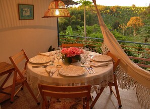 A round table set for four with lace tablecloths, a vase of pink flowers, and a hammock attached to the balcony railing. - Finca Turistica Machangara (Quimbaya)