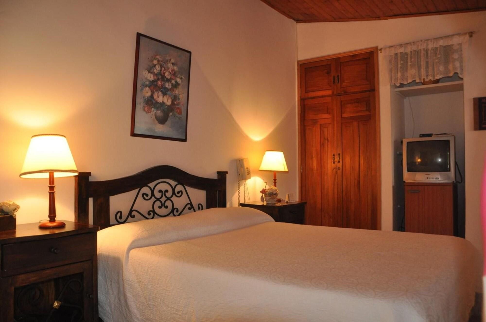 Un dormitorio con una cama, dos lámparas de noche, un armario de madera, un televisor y un cuadro floral en la pared.