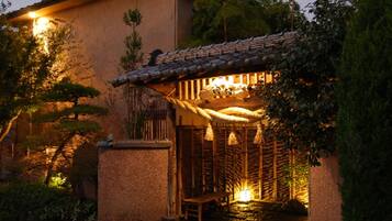 Een traditioneel Japans gebouw met pannendak, een houten bankje en een klein waterpartij.