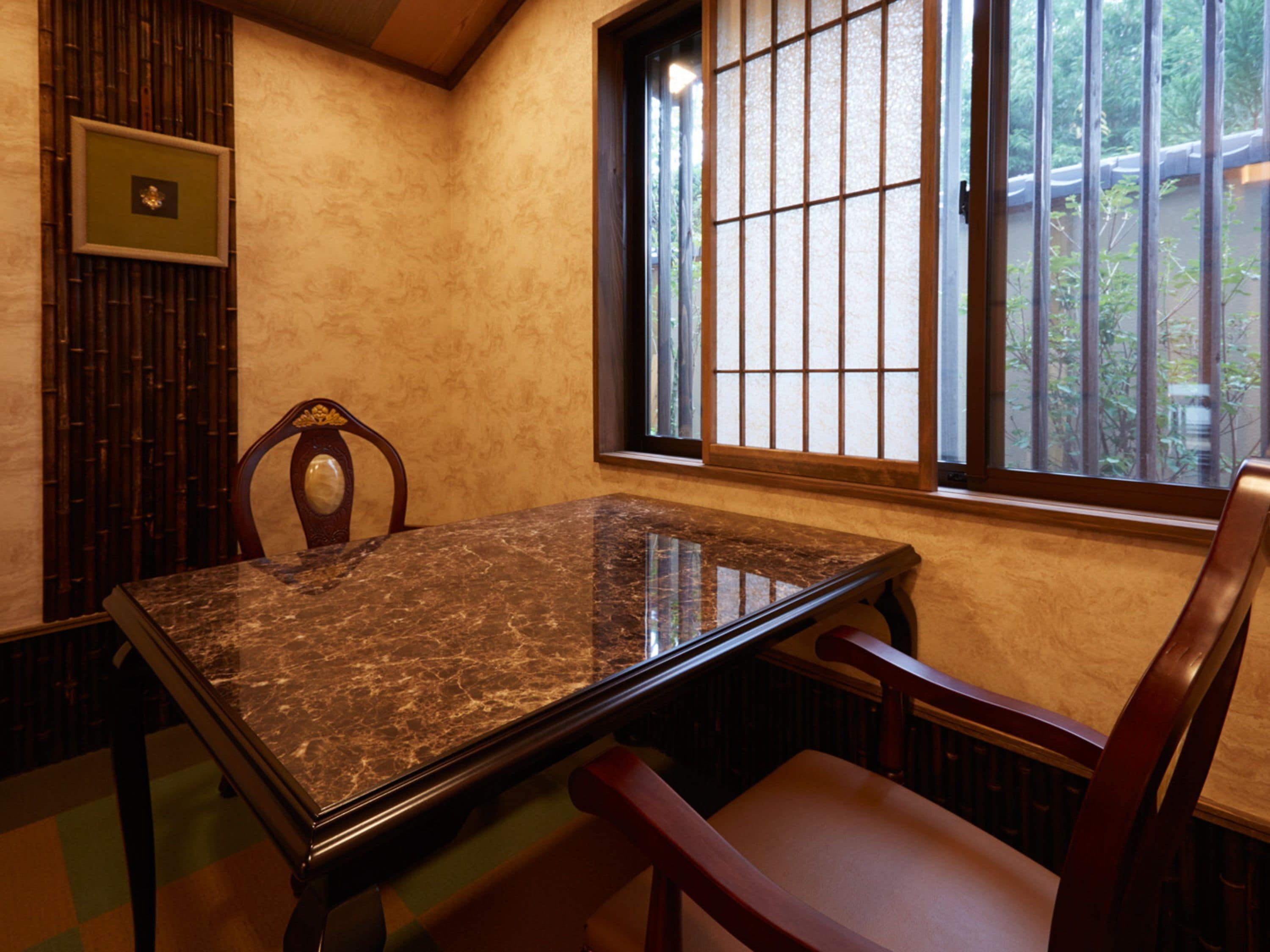 A room with a marble table, wooden chairs, a window with bars, and a bamboo screen.