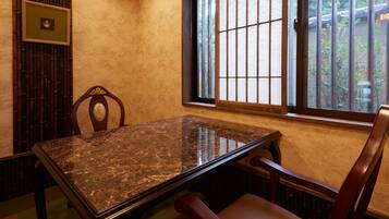 A room with a marble table, wooden chairs, a window with bars, and a bamboo screen.