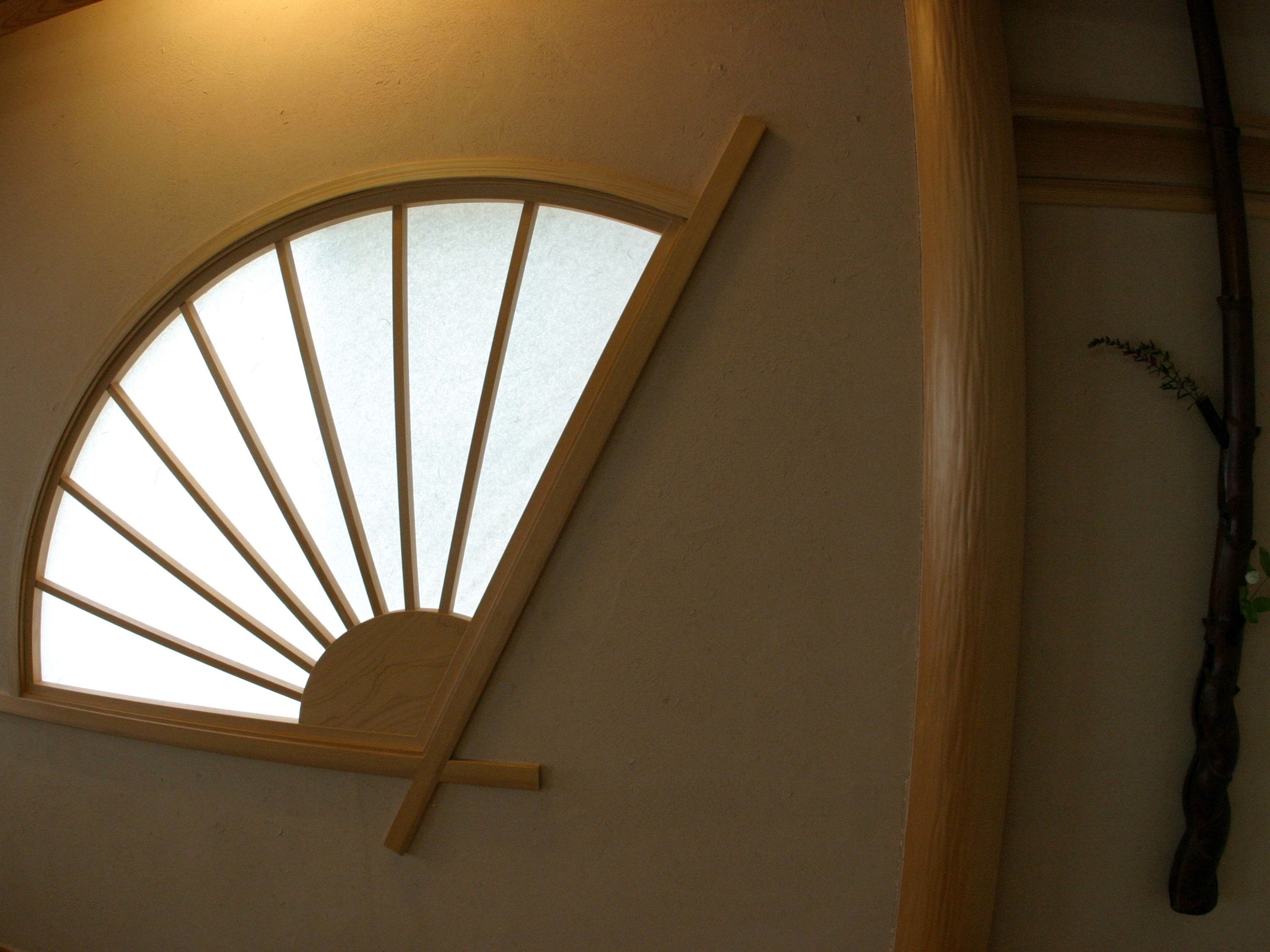 Una habitación con un ventanal en forma de abanico de madera, una viga de madera y una planta en la pared.